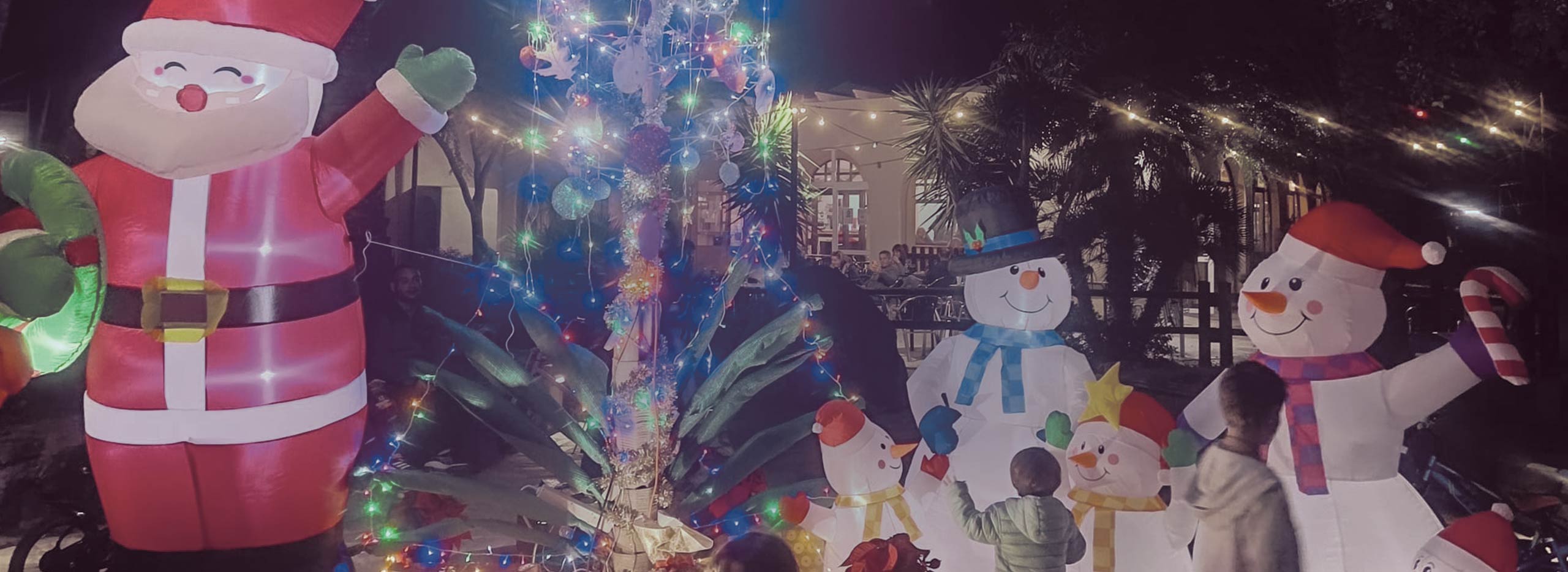Exterior del Camping Los Escullos con una pita con luces de navidad, muñecos de nieve y un Papá Noel hinchable, algunos niños juegan alrededor